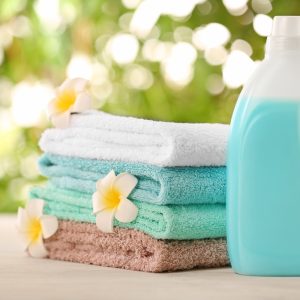 Pile of fresh towels, flowers and detergent on table against blurred background